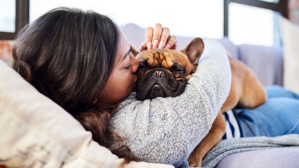 A woman lays on her couch snuggling with her dog.