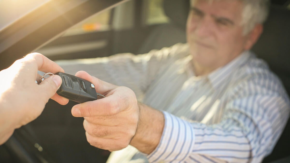 An older man hands his car keys to someone.