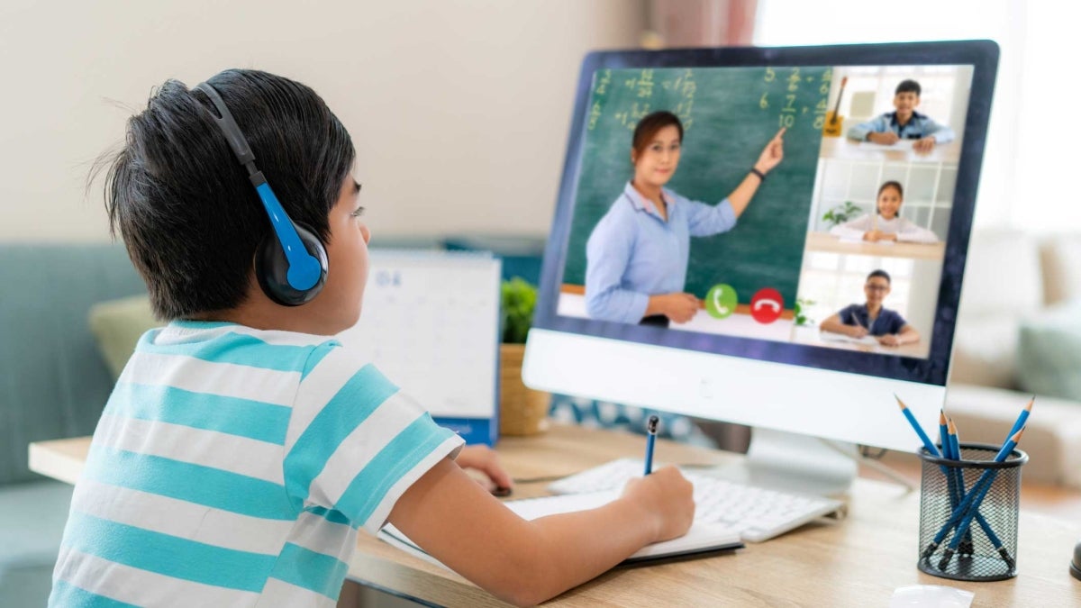 A young student watches his teacher on the laptop screen