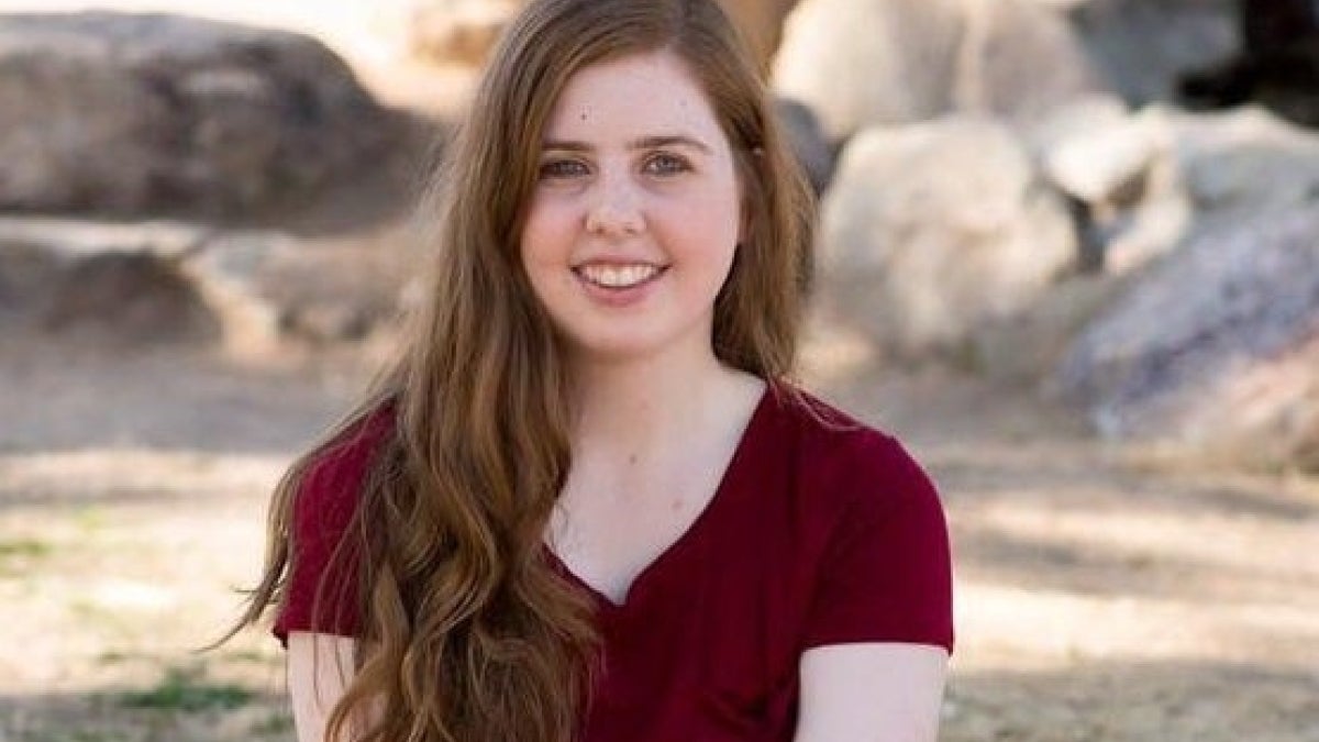 Kathleen Tucker is pictured in a red shirt with her hair on her shoulder with a muted rockscape background.