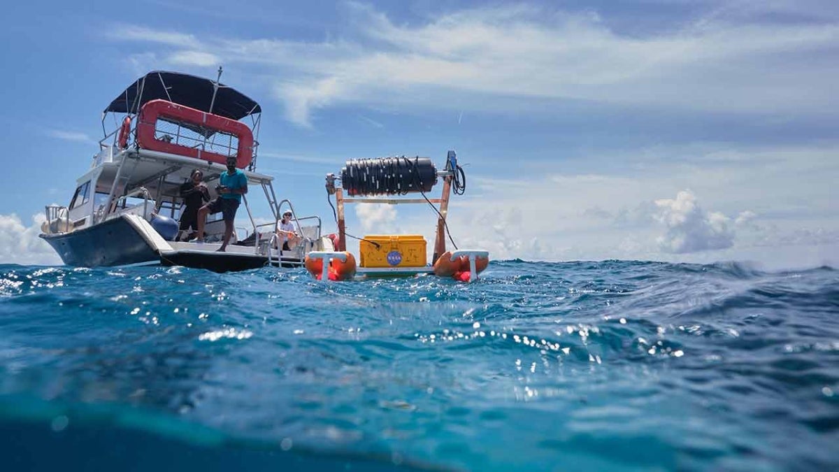 ASU alumnus and student stand on a boat and launch aquatic robot