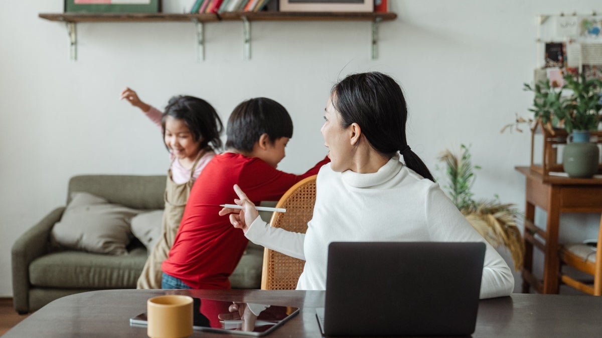 Woman turning around from computer to talk to playing kids at home.