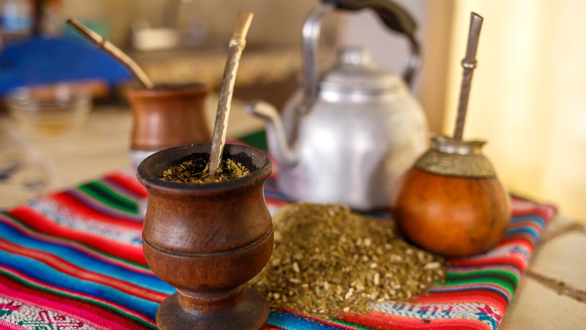 A collection of drinking-related items on a blanket and table, including teapot, goblet, herbs, cups and straws.