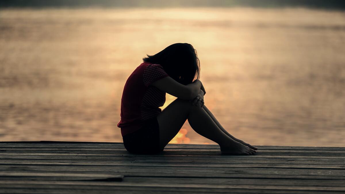 Girl sitting on dock with head down on knees