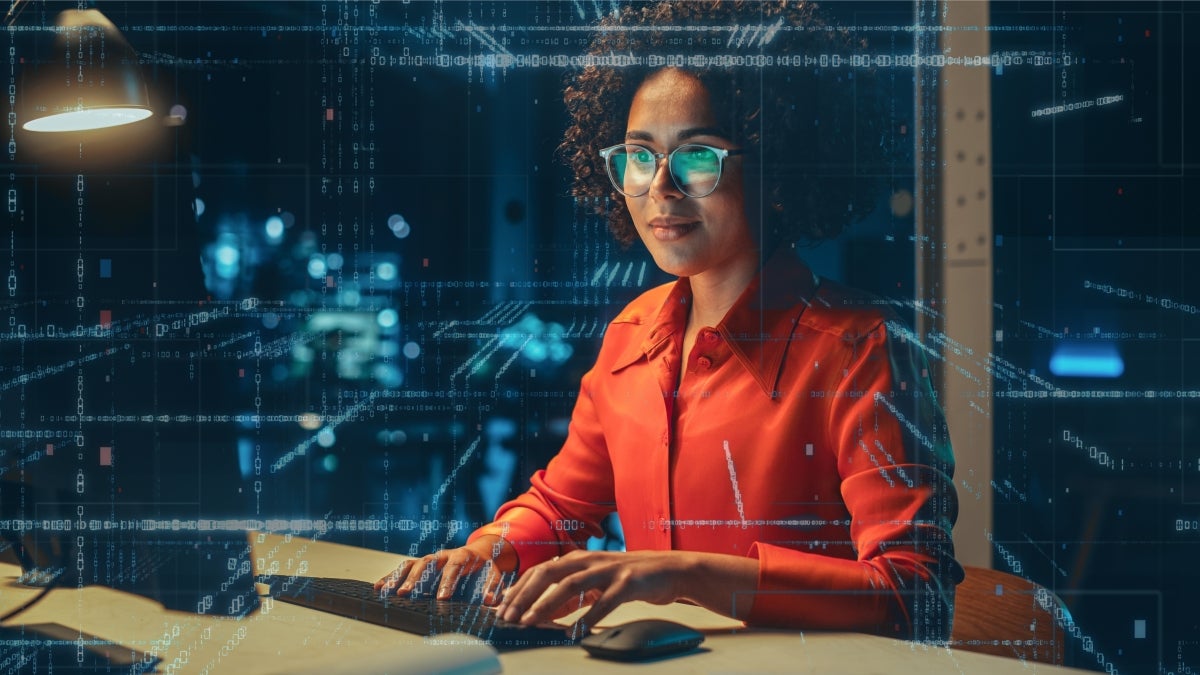 Women at a computer with abstract digital coding overlayed on top of the image.