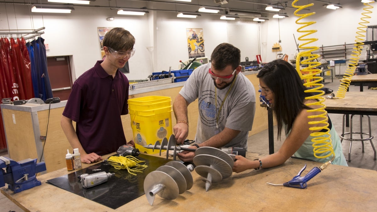 Photo of three students attaching an auger to a drill