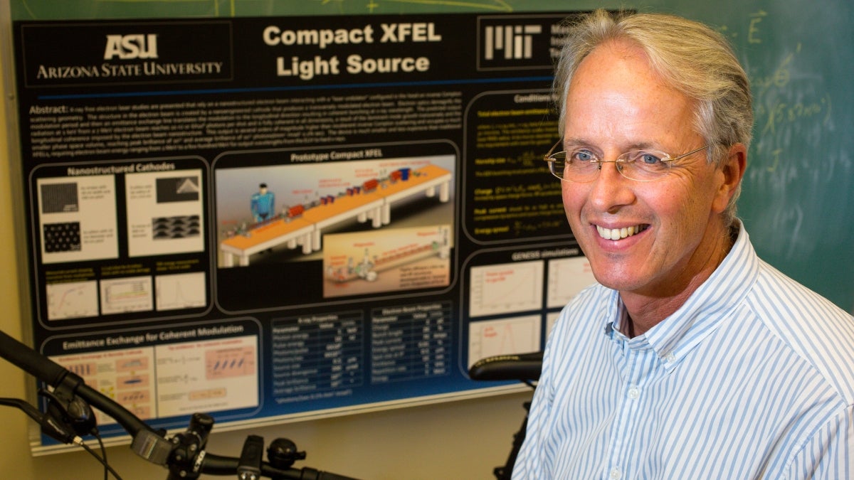 Man poses in front of an X-ray laser display poster