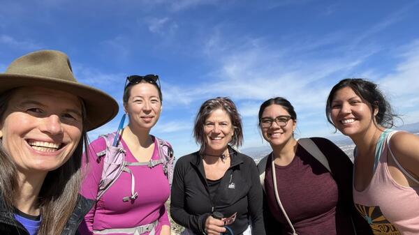 Nancy Grimm and ESSA (Earth Systems Science for the Anthropocene) scholars smile against a blue sky background while on a hike. 