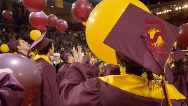 graduates in caps and gowns watching balloons drop at graduation