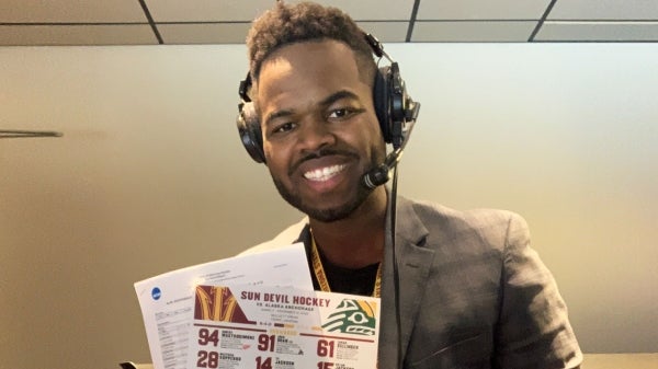 Trey Matthews smiling at the camera holding papers and wearing headphones.