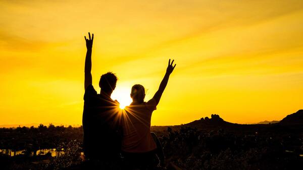 Silhouetted people hold up pitchfork gestures against a setting sun