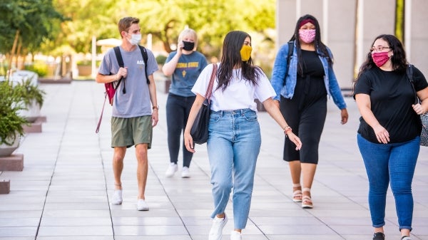 Students walk on a sidewalk while distancing and wearing face coverings