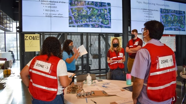 A group of people confer around a map on a large screen at Sun Devil Stadium during the Maricopa County Serosurvey.