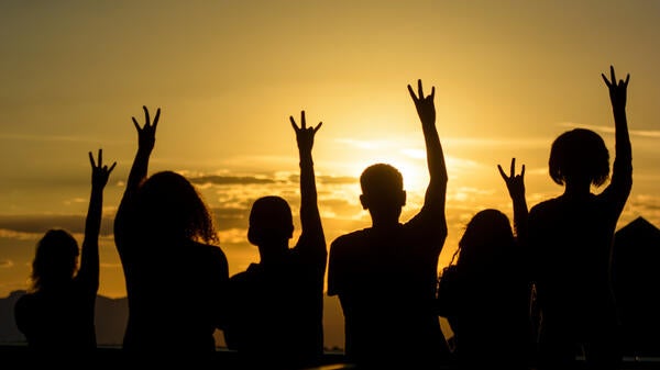 students with hands in air making pitchfork sign in front of sunset