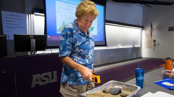 A woman points a thermometer at a pan of dirt and stones that had been outside for 90 minutes