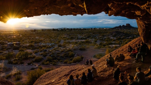 People sit on the side of a hill looking at the sunset