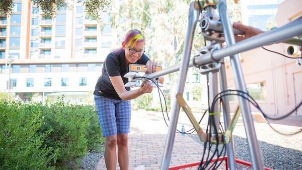 Woman using technical equipment to record shade temperatures outdoors.