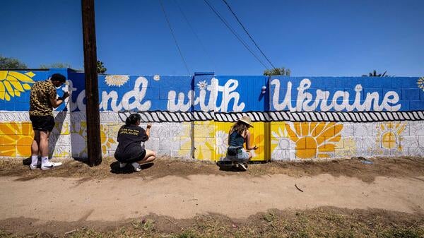 People painting a mural on a wall that says "Stand with Ukraine"