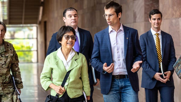 A man and a woman talk while leading a group of people down an outdoor hallway