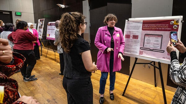 People talking and standing in a hallway where several posters are on display.