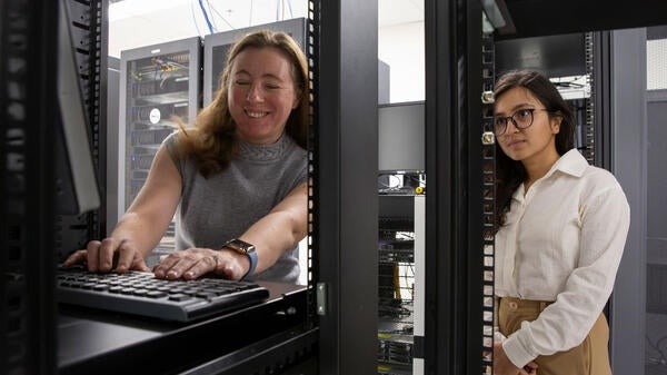 Woman working on a computer as a student watches.