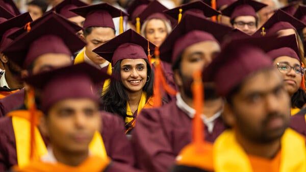 Students in graduation caps and gowns sit in an audience