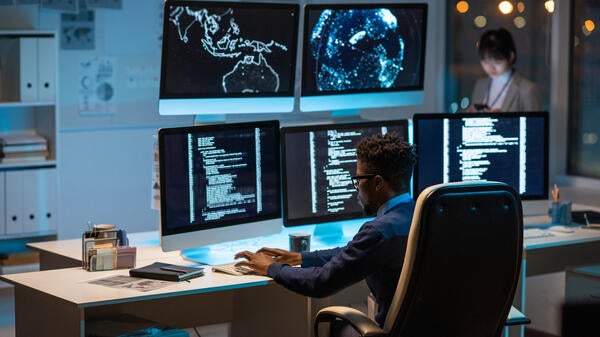 Person sitting in front of several computer screens.