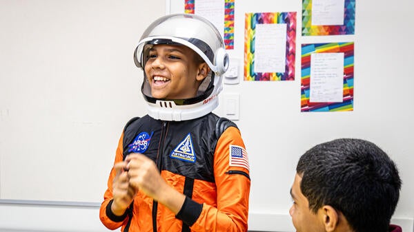 A boy wearing an astronaut costume smiles wide at someone off camera