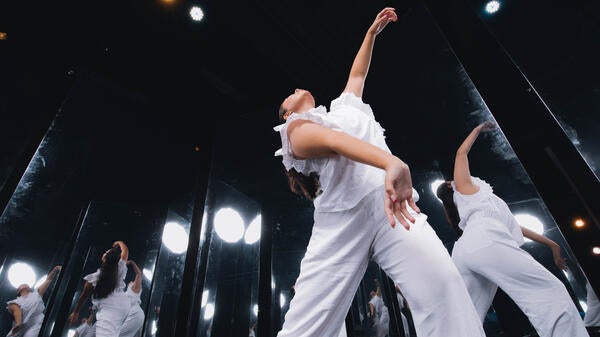 A dancer in white gestures in front of mirrors