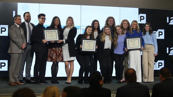 Groups of students holding three framed certificates on a stage