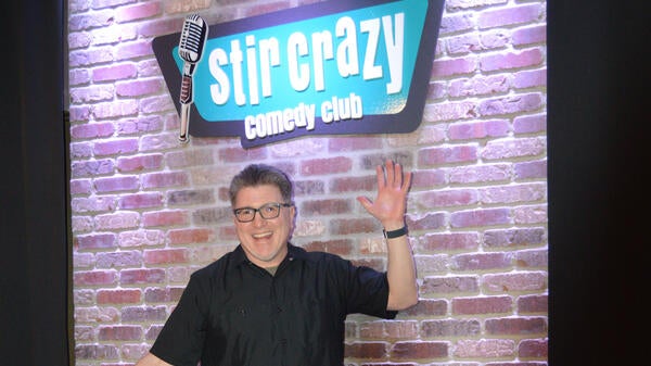 Man standing in front of a sign that reads "Stir Crazy Comedy Club."