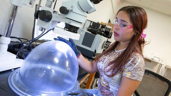 A woman works with an anti-fog coating on a spacesuit helmet