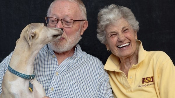 A man and a woman laugh while holding a dog