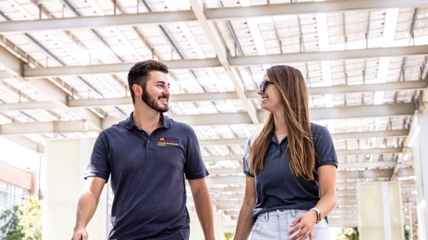 Male and female student wearing ASU sustainability practices polos walk under solar panels on campus