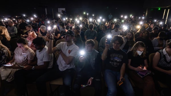 A crowd in a darkened room hold up their phone flashlights