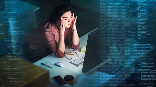 Person sitting in front of computer screen with head in their hands with coding swirling around them