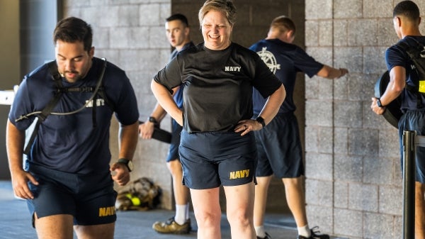 Woman in Navy workout gear smiles as she coaches recruits.