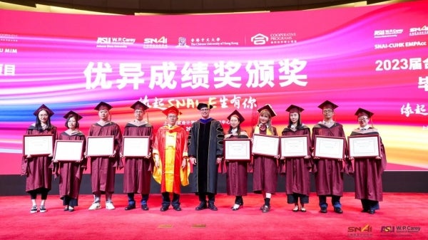 Group of people standing on a stage wearing graduation regalia.