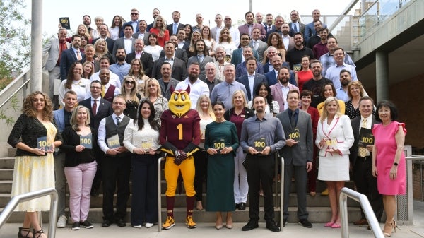 A large group of people on outdoor stairs holding plaques with Sparky in the center.