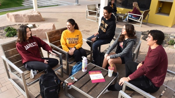 Students wearing Arizona State University clothing gathered in a circle talking.