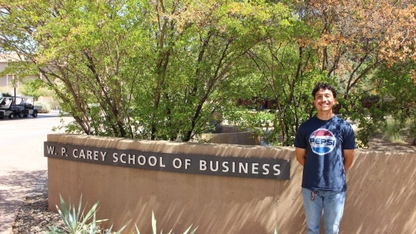 Student Joseph Espinoza stands smiling outside in front of the W. P. Carey business school sign