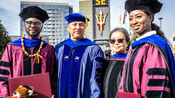 Four people in graduation gowns smile at the camera