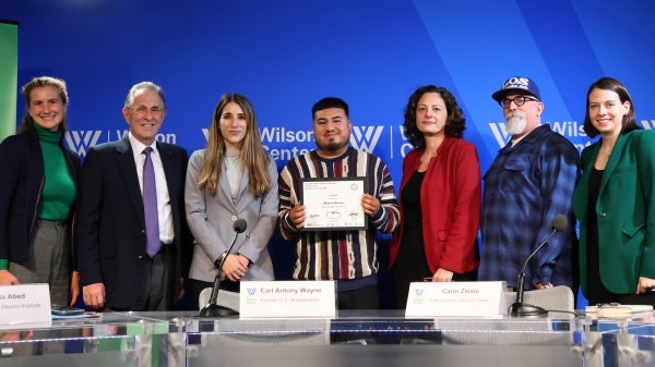 Seven people stand in a line smiling for the camera, a man in the center holding an award. 