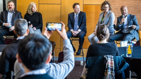 Group of people seated on stools at the front of a room speaking to an audience.