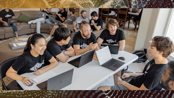 A group of ASU students sit around a table on laptops talking and smiling