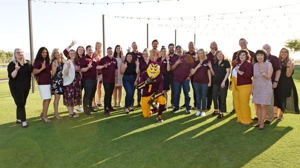 A group of people stand outside posing with Sparky.