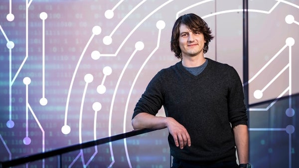 Director of Center for Cybersecurity and Trusted Foundations Adam Doupé leaning on a railing with digital circuit designs in the background.