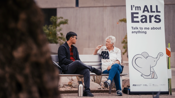 A young man and an older woman sit on a bench, talking