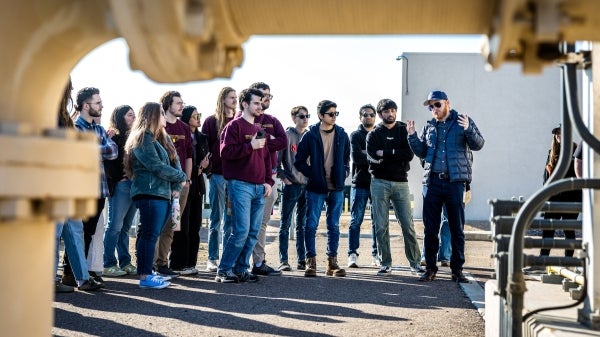 Group of people gathered outside looking to someone in front mid-speech