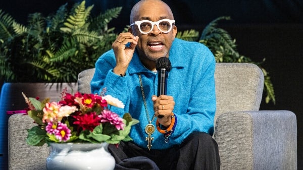 Filmmaker Spike Lee speaks into a microphone while siting on a couch on stage during a lecture event